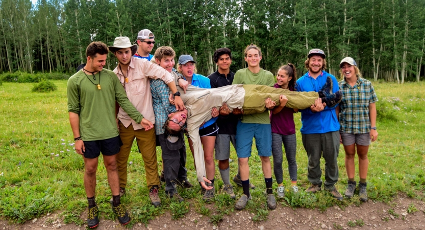 A group of students hold another up who is laying across them. 